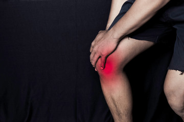 Asian Man Holding his knee. He feels pain on his knee with black background. Joint inflammation or healthcare concept