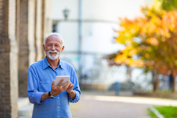 Senior man uses his digital tablet. Happy senior man holding digital tablet. Senior businessman using touchpad at outdoor. Senior businessman holding touchpad