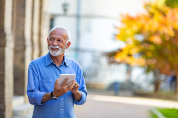 Senior man websurfing on tablet outside the house. Senior mature man walking using tablet pc. Senior man uses his digital tablet. Older man using tablet computer in park.
