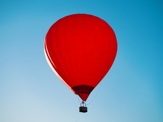 Red hot air balloon with wicker basket flying at blue sky background at sunny day