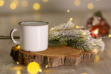 Decoration for New Year's holidays. Warm cozy atmosphere. White metal mug on a wooden stand, next to a snowy Christmas tree branch.