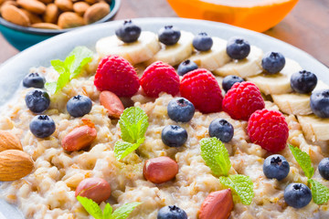 Bowl of oatmeal porridge with berries, honey and fruits on burlap. Tasty oatmeal with raspberries, blueberries and nuts on wooden boards. Healthy breakfast
