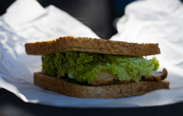 Sandwich of white toast bread with greens, cabbage, turkey meat and sauce in white kraft bag. Snack food.