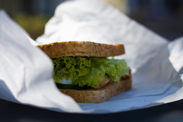 Sandwich of white toast bread with greens, cabbage, turkey meat and sauce in white kraft bag. Snack food.