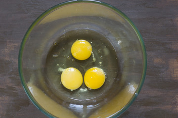 Three raw chicken yolks and whites in glass bowl on the wooden table