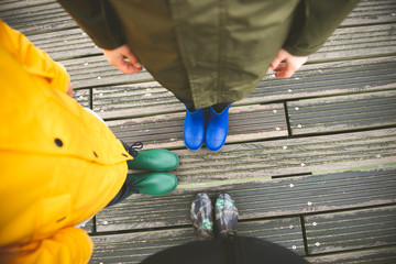Family of three standing on woode pier in high rubber boots