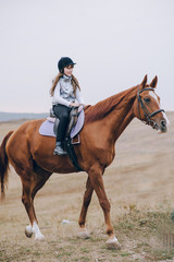 Obraz premium First lessons of horseback riding. Young beautiful girl riding a horse in a field.