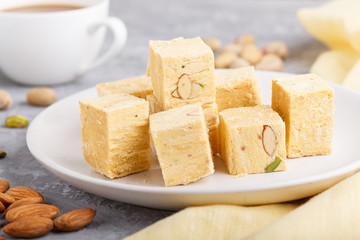 traditional indian candy soan papdi in white plate with almond and pistache on a gray concrete background. side view, selective focus.