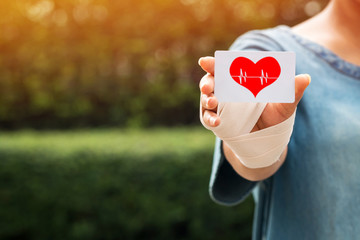 Patient woman with a bandage on her hand are holding and show a white credit card and red heart...