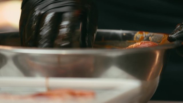 Professional chef marinating meat in a metal bowl in the kitchen of a fancy restaurant