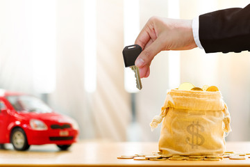 Investor hand hold a car key submit to each other a car model and money bag in the office, The...
