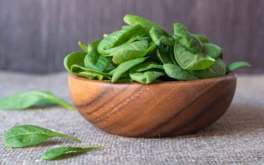 fresh green spinach leafs in a wooden bowl, isolated on wooden background