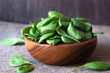 fresh green spinach leafs in a wooden bowl, isolated on wooden background