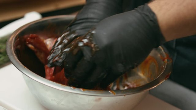 Professional chef marinating meat in a metal bowl in the kitchen of a fancy restaurant
