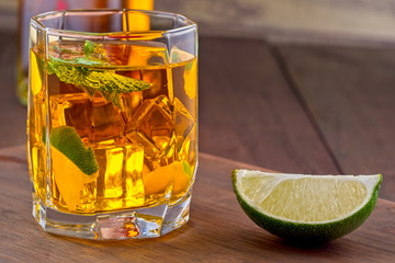 Alcoholic cocktail with ice and lime wedge on a wooden tray