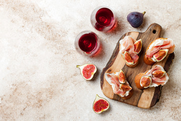 Crostini with prosciutto, cream cheese and figs on wooden board. Appetizers, antipasti snacks and red wine in glasses. Authentic traditional spanish tapas set. Light beige background. Top view