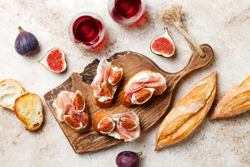 Crostini with prosciutto, cream cheese and figs on wooden board. Appetizers, antipasti snacks and red wine in glasses. Authentic traditional spanish tapas set. Light beige background. Top view