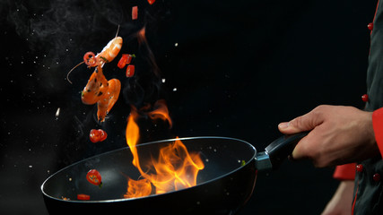 Closeup of chef holding wok pan with falling prawn - obrazy, fototapety, plakaty