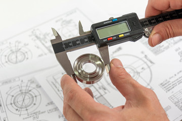 Measurement of a turned part. Electronic caliper in the technician's hand. A round steel piece in the jaw of a measuring tool with a blurred technical pattern on the background. Engineering.