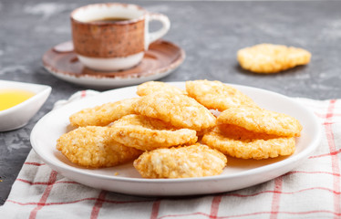 Traditional japanese rice chips cookies with honey and soy sauce on a white ceramic plate and a cup of coffee on a black concrete background. side view, selective focus.