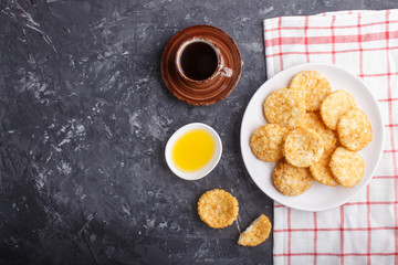 Traditional japanese rice chips cookies with honey and soy sauce on a white ceramic plate and a cup of coffee on a black concrete background. Top view