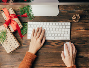 Top view on female hands on a computer keyboard at a computer. Gift boxes lie on a wooden table. Season of discounts and online gift orders. Delivery of online orders.