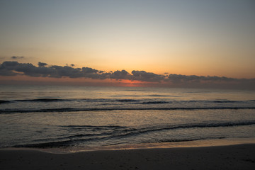 Sunrise. Dawn on the Mediterranean coast, Tunisia Sand in the foreground, small waves, the sun above the horizon, long clouds