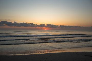 Obraz premium Sunrise. Dawn on the Mediterranean coast, Tunisia Sand in the foreground, small waves, the sun above the horizon, long clouds