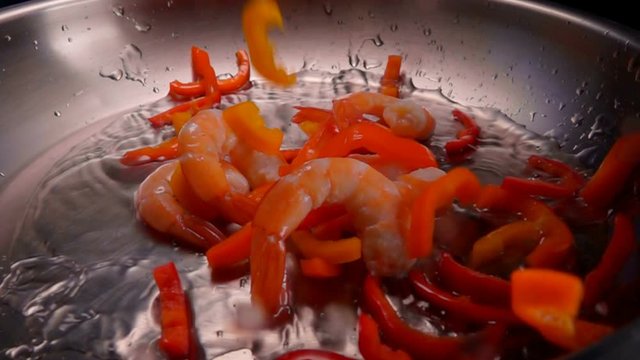 Bunch of Shrimps and red pepper fall into the steel pan on a heated vegetable oil