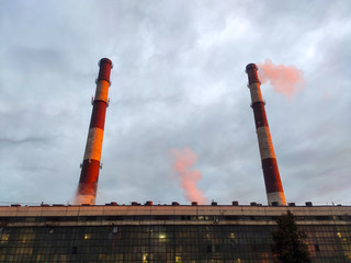 pipes over a plant with steam coming out against the sky. at sunrise in the red light of dawn