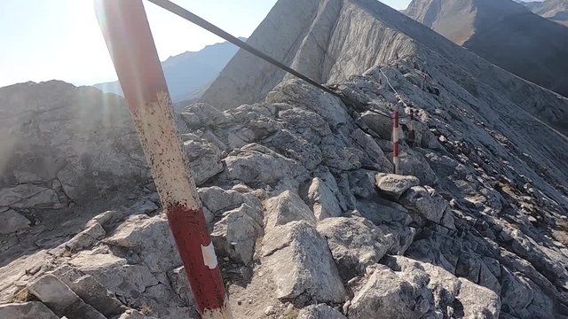 A woman walks along the edge of a mountain ridge and holds on to a steel rope.