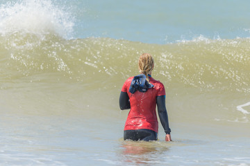 woman standing in the water facing the waves. surf instructor wearing a red shirt so she is easy to recognize by her pupils