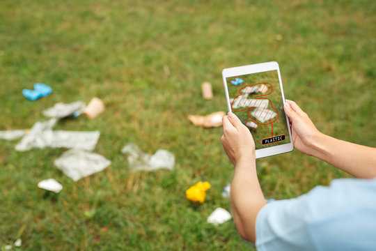 Waste Management. Young girl sitting a park holding smartphone using app for litter recognition and sorting plastic identified on screen close-up