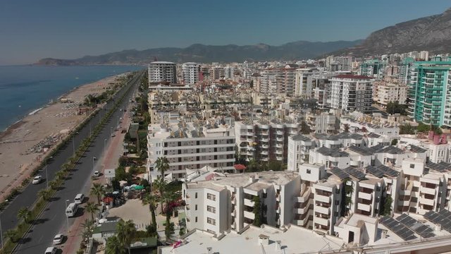 Panoramic aerial view of urban landscape, coastline and beaches from Mahmutlar to Alanya Castle on the Turkish Mediterranean Coast. Tourists enjoy the beach & watersports. The busy D400 runs longside.