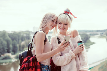 young pretty woman posing in the street with phone, outdoor portrait, hipster girls, sisters, chic, tablet, internet, using smartphone, close-up fashion model, post in social cell, holding, selfie,USA