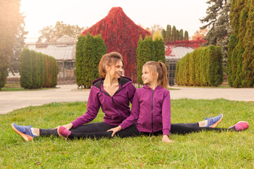Outdoors leisure. Sisters doing exercise side splits in the autumn park looking at each otehr happy