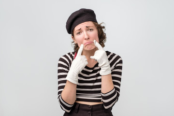 Young upset mime woman making fake smile with her fingers stretching the corners of her mouth. Try to stay positive after failing at something.