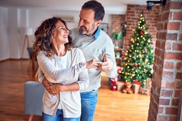 Middle age beautiful couple smiling happy and confident. Standing and dancing around christmas tree at home