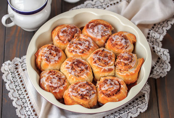 Homemade cinnamon buns . Cinnamon rolls drizzled with vanilla icing in baking dish. Dark wooden background, selective focus.