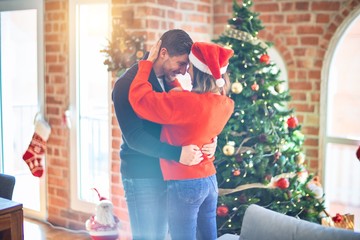 Young beautiful couple smiling happy and confident. Standing and hugging around christmas tree at home