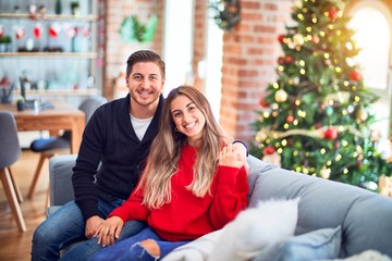 Young beautiful couple smiling happy and confident. Sitting on the sofa hugging around christmas tree at home