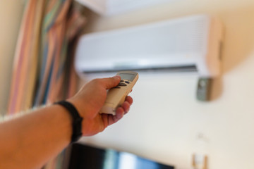 In male hands of the remote control air conditioning in the hotel room. Cooling and airing in the hotel room. Close-up view of the use of some electrical appliances such as air conditioning.