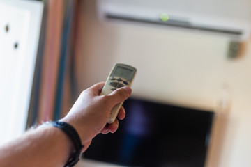 In male hands of the remote control air conditioning in the hotel room. Cooling and airing in the hotel room. Close-up view of the use of some electrical appliances such as air conditioning.