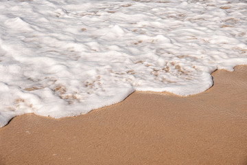 Soft waves with foam of ocean on the sandy beach background