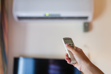 In female hands of the remote control air conditioning in the hotel room. Cooling and airing in the hotel room. Close-up view of the use of some electrical appliances such as air conditioning.