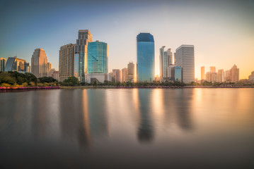 Fototapeta na wymiar Lake in Public Park under Skyscrapers at Sunrise. Benjakiti Park in Bangkok, Thailand