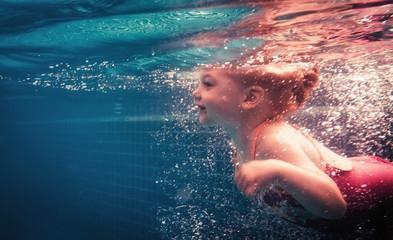 Happy child swimming underwater in swimming pool during diving training. 