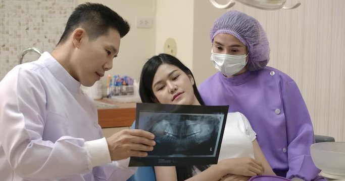 Dentist showing teeth x-ray image to patient. Dentist and patient choosing treatment in a consultation with medical equipment in the background.