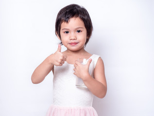 Little asian cute girl 3 years old holding and drinking milk from glasses with trumps up over white background. Milks is essential and nutrition for the child's body.