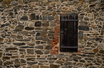 Fototapeta na wymiar Ancient fortress wall made of various stones. There is an aged brown wooden door in the wall. Background.